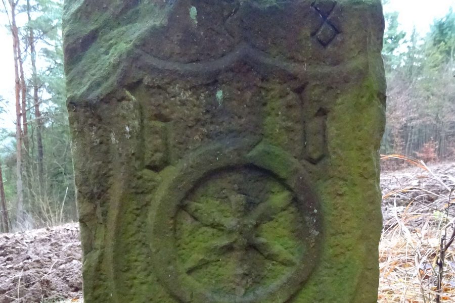 Grenzstein von 1508 im Wald, mit Wappenschild und Rad