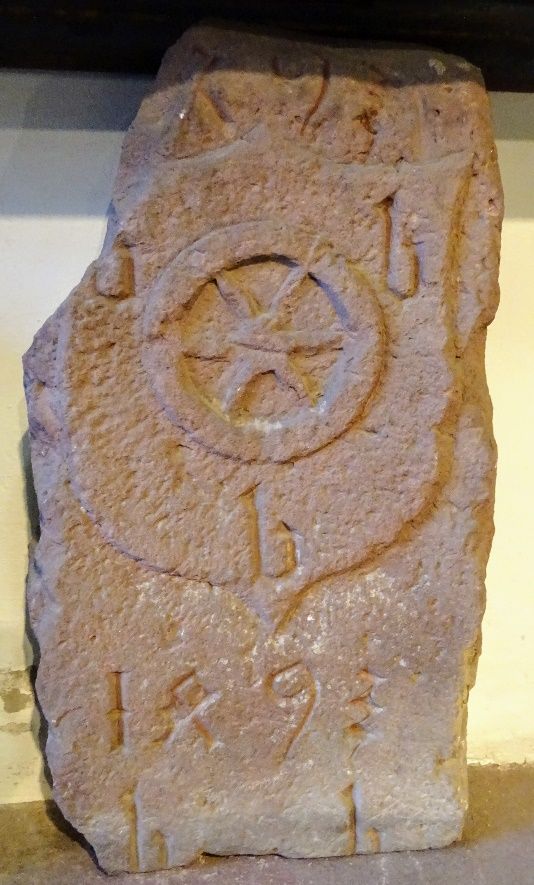 Behauener Grenzstein mit Wappenschild, Mainzer Rad, drei b und der Jahreszahl 1493 in einem Museum.